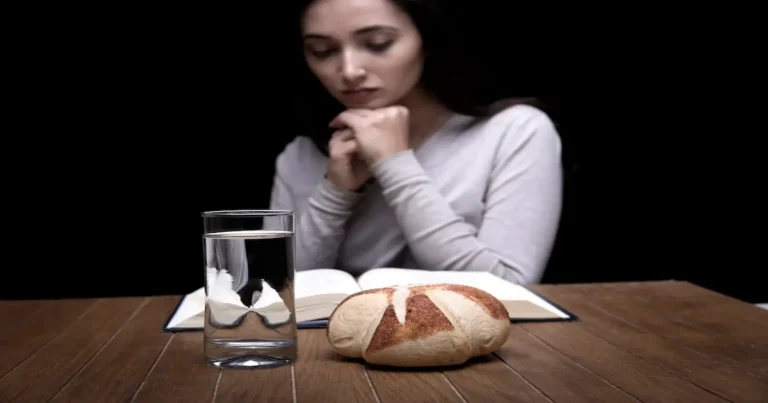 Mujer en ayuno junto a una biblia, un vaso de agua y un pan